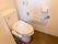 ライトブラウンのフローリングと白い壁のトイレがある。壁には手すりが設置され、温水洗浄便座が付けられている。