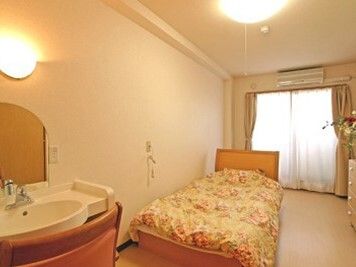 手前に洗面台、奥の方にベッドと緊急コールがある施設内の居室