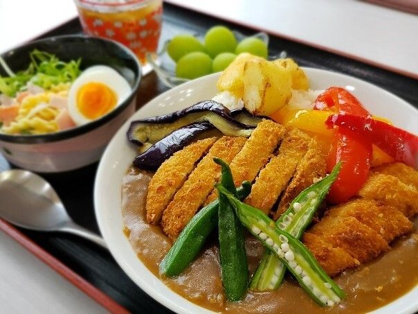 野菜とカツのカレーとサラダ、マスカット、お茶が乗ったトレー
