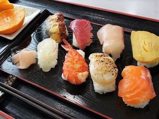 サーモンやまぐろなどのお寿司とみかん、箸が乗ったトレー