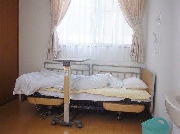 窓の下には布団が敷かれたベッドが置かれ、ベッドの上には緊急通報装置を設置している。