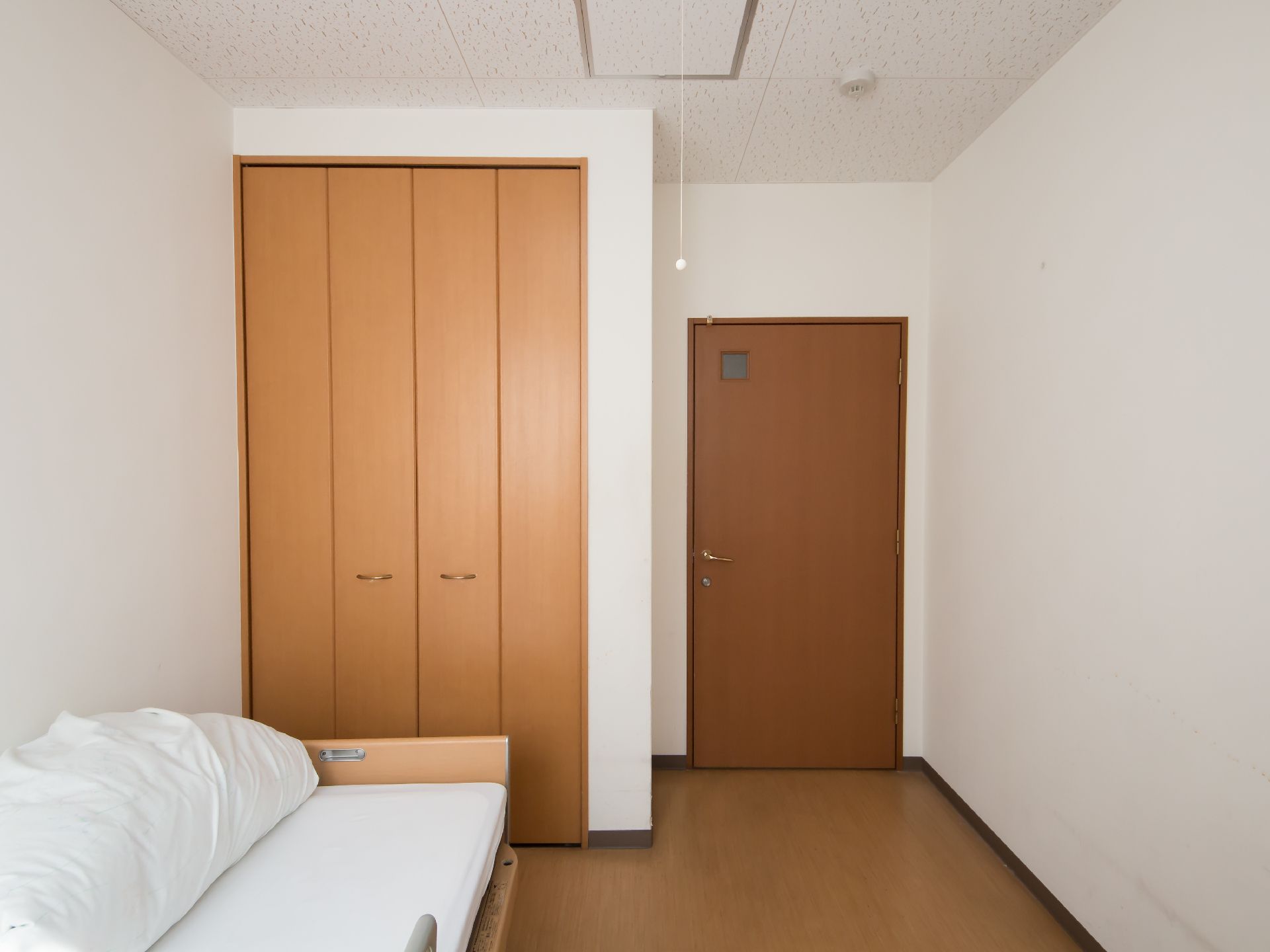 右奥に木製の扉の入口がある。左手に折れ戸式のクローゼットがあり、天井近くまで高さがある。壁際にソファがある。