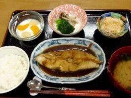 魚の煮つけや野菜の和え物、みそ汁や白いご飯、デザートがそれぞれの器に盛られている。