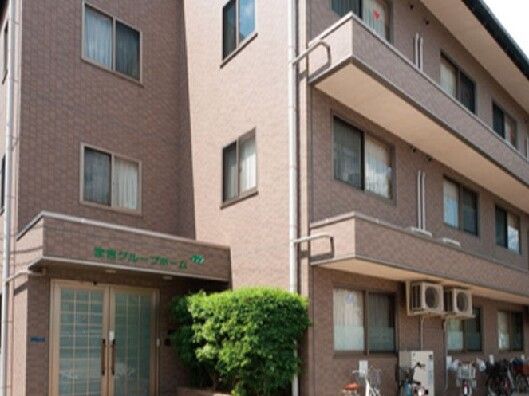 ブラウン系の外壁の３階建ての建物は日当たりがよく、玄関先の屋根にはホーム名が書かれている。