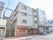 施設は4階建て。道路に面していて車を寄せるスペース分セットバックしてある。ドアにはひさしがある。車寄せの隅にベンチがある。