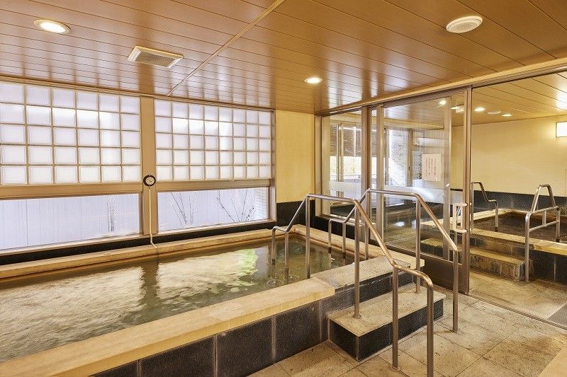 茶色の長テーブルと椅子が設置されている。等間隔で上部からライトがある。室内壁際には観葉植物が置かれている。