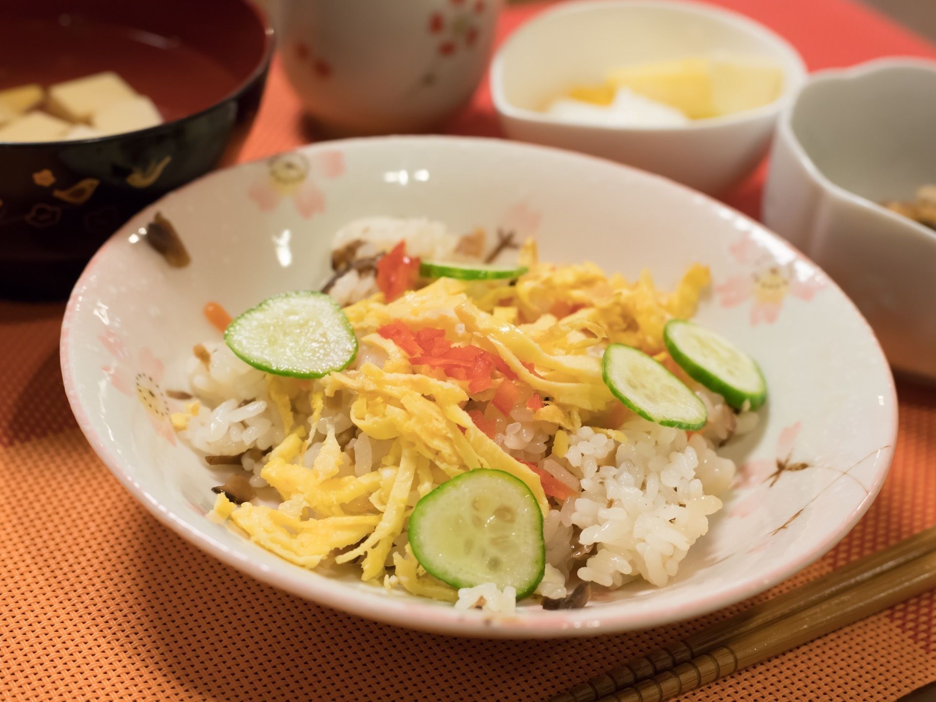 さくら模様の華やかな器に、ちらし寿司が盛り付けられている。酢飯の上に、緑のきゅうり、黄色いたまご、赤い紅ショウガが彩りよくのせてある。