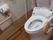 トイレの左右には、ベージュ色の大きな手すりが取り付けられている。左側の壁にはペーパーホルダーがあり、三角形に紙が折ってある。