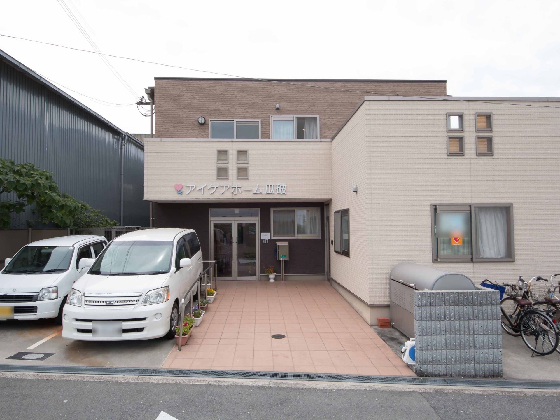 施設は、大きめの一戸建てのような印象を受けるものである。玄関先に駐車スペースがあり、足の不自由な方も通行しやすいようバリアフリー仕様である。