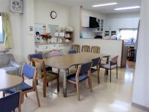 椅子と机、キッチンがあるリビング。施設内にあるリビングの様子