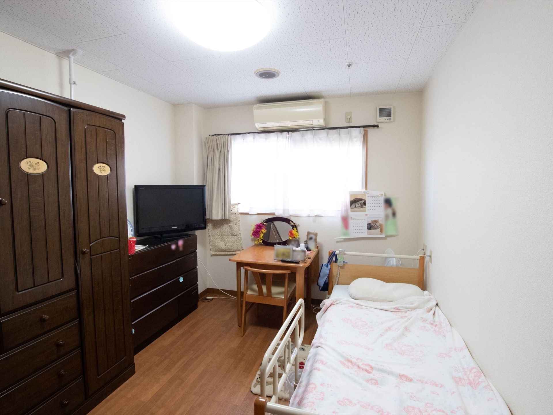 ベッドには手すりが設置されている。小さな机と椅子があり、鏡や写真を飾っている。タンスやチェストが置かれており、テレビ鑑賞もできる。
