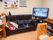 黒い大きなソファが置かれたリビングダイニング。。すぐそばにテレビがあり、ソファにはひざ掛けなども置かれている。