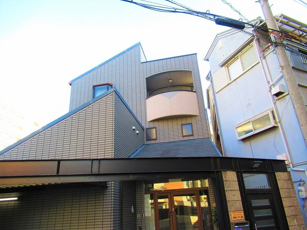 ブラウン系の建物は重厚感があり、ベランダも付いている。玄関には屋根が付き、自動ドアも設置されている。