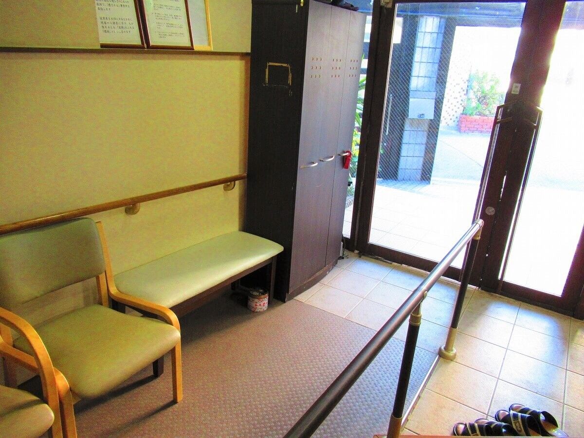 手すり付きのスロープが設置され、いすやベンチが置かれた玄関内部。大きなドアが付き明るい。