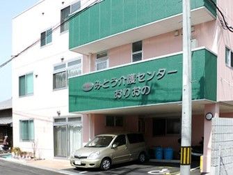 ３階建ての建物の１階部分には駐車スペースも。２階部分と３階部分にはベランダがあり、２階のベランダ部分に「みとう介護センターおりおの」と書かれている。