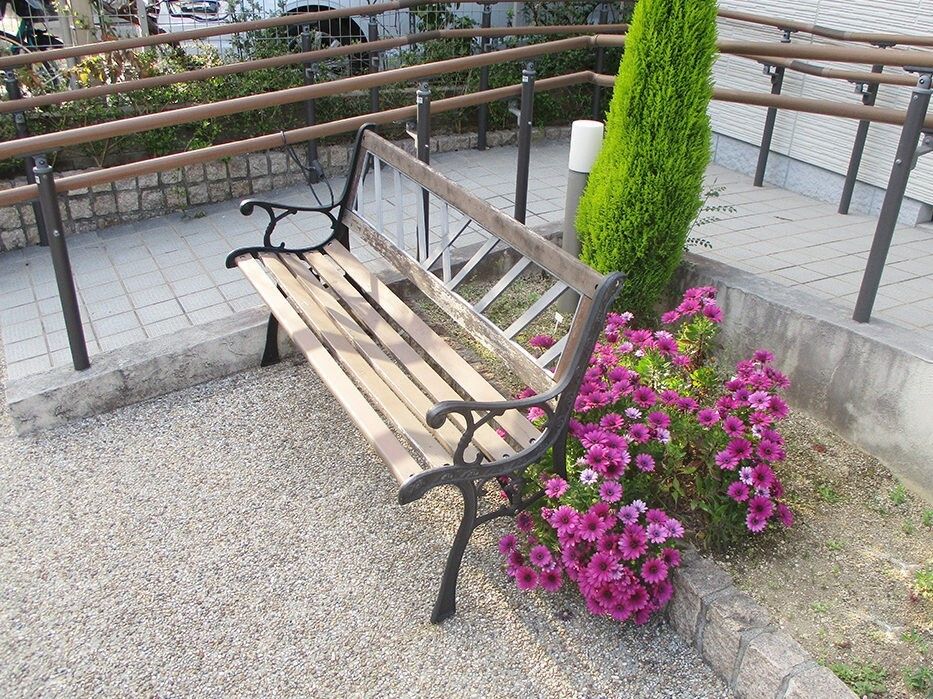 手すり付きのスロープが付いた玄関の前には木製のベンチもあり、季節の花や木も植えられている。