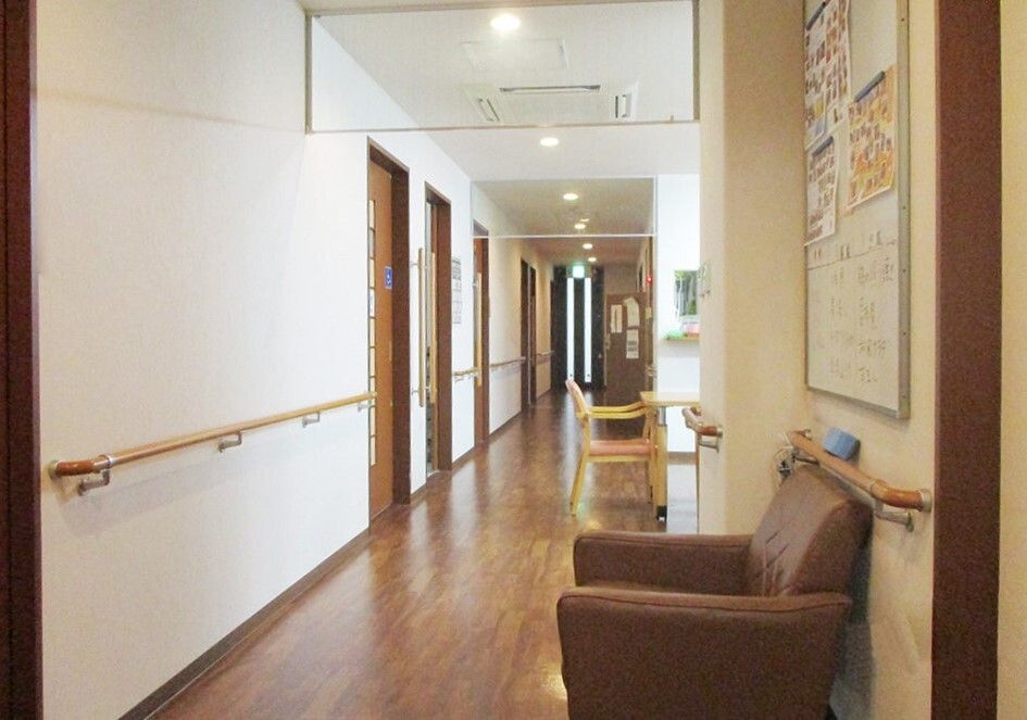 左側には居室のドアが並び、右側手前にはソファとホワイトボードが置かれ、手すりが両サイドについている。