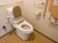 温水洗浄便座が取りつけられたトイレで、タンクに背もたれ用パットが設置されている。壁に操作パネルがある。