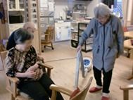 掃除で共有スペースの掃除をしている女性入居者とそれを見ている２名の入居者。