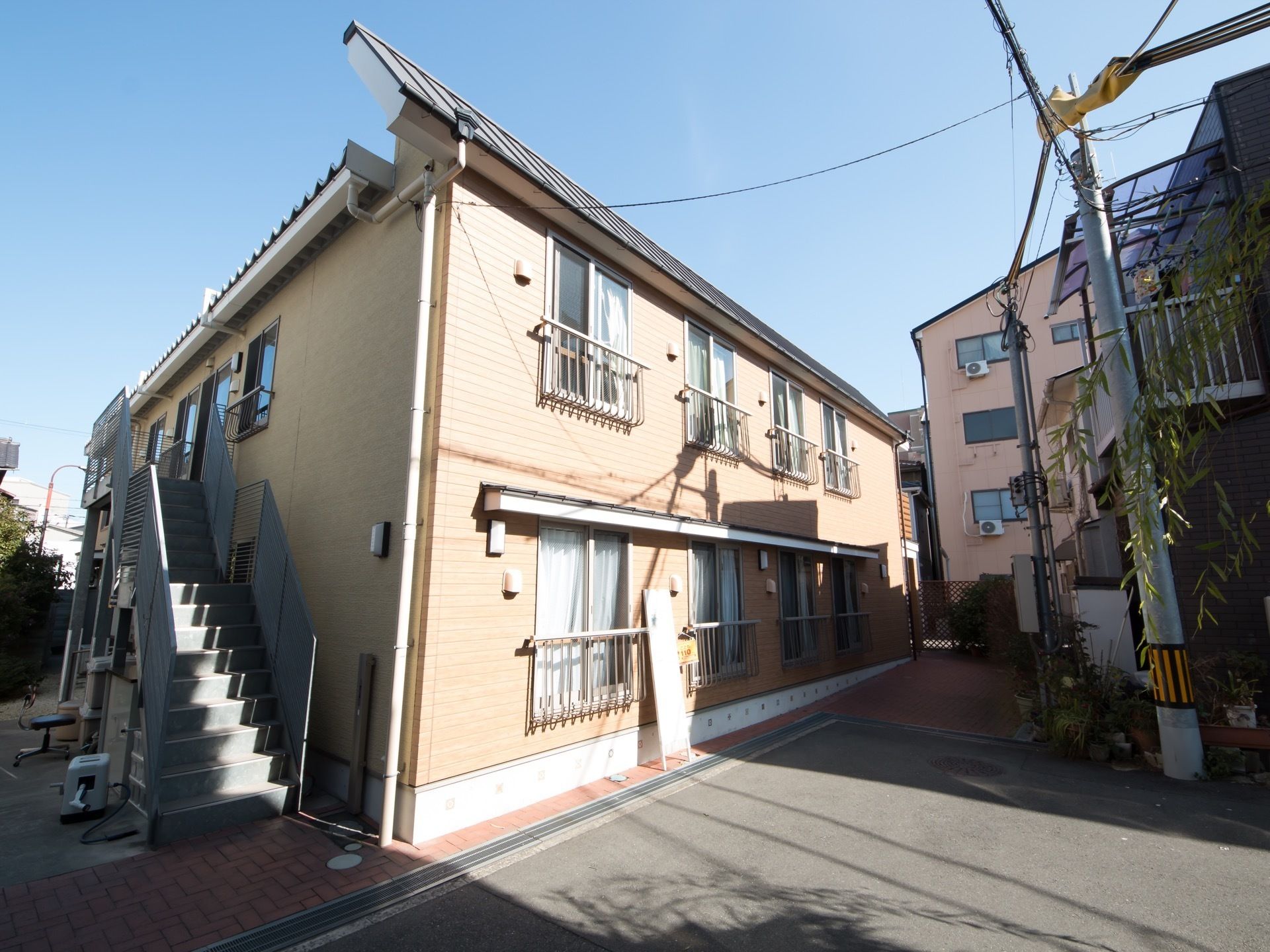 ベージュ色を基調とした外壁の２階建ての施設である。両側に手すりがついた灰色の非常階段が設置されている。