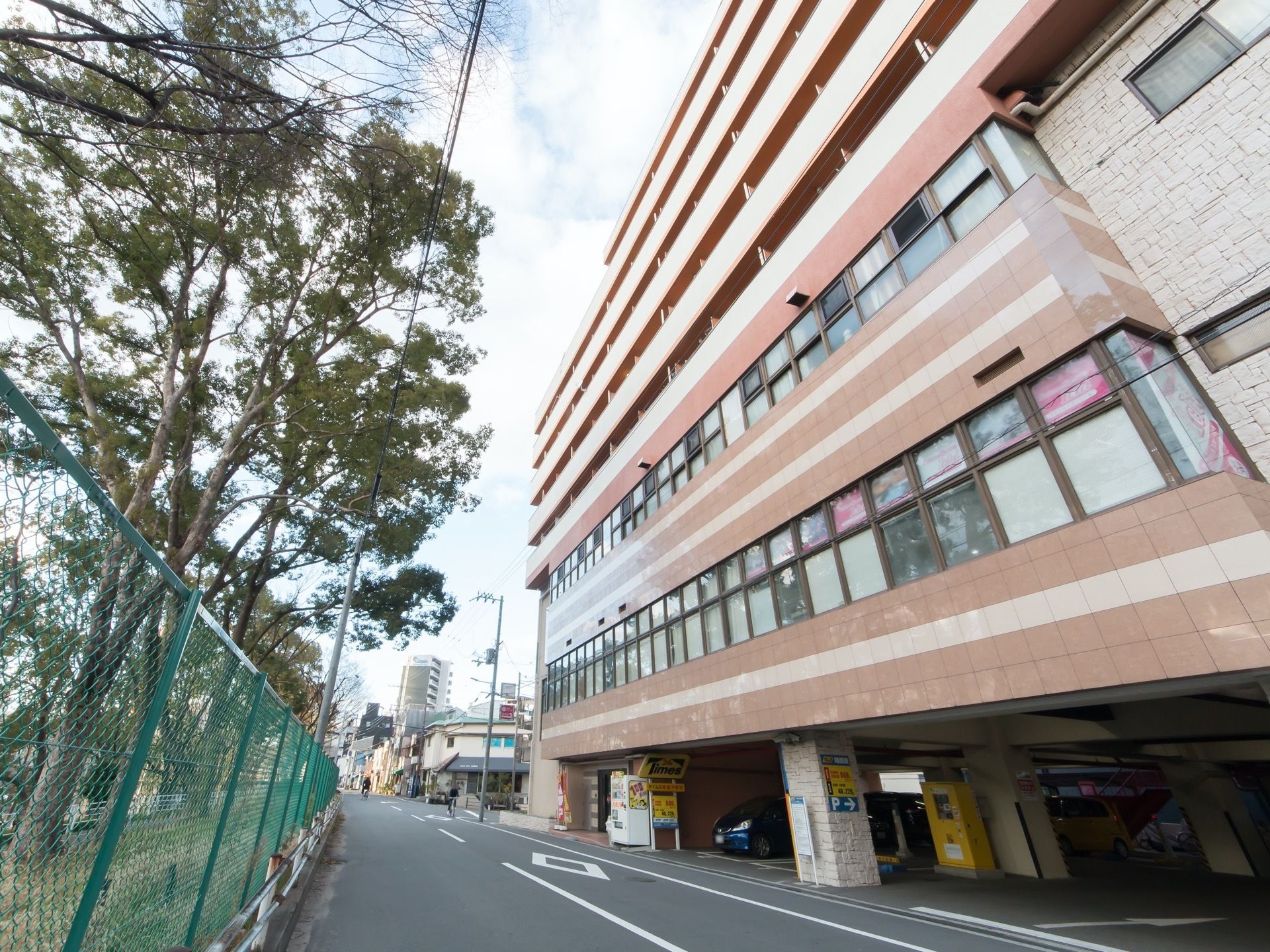 ブラウンを基調としたマンションのような外観のグループホーム。地上１階部分には駐車場が設けられており、複数台の車が停められている。