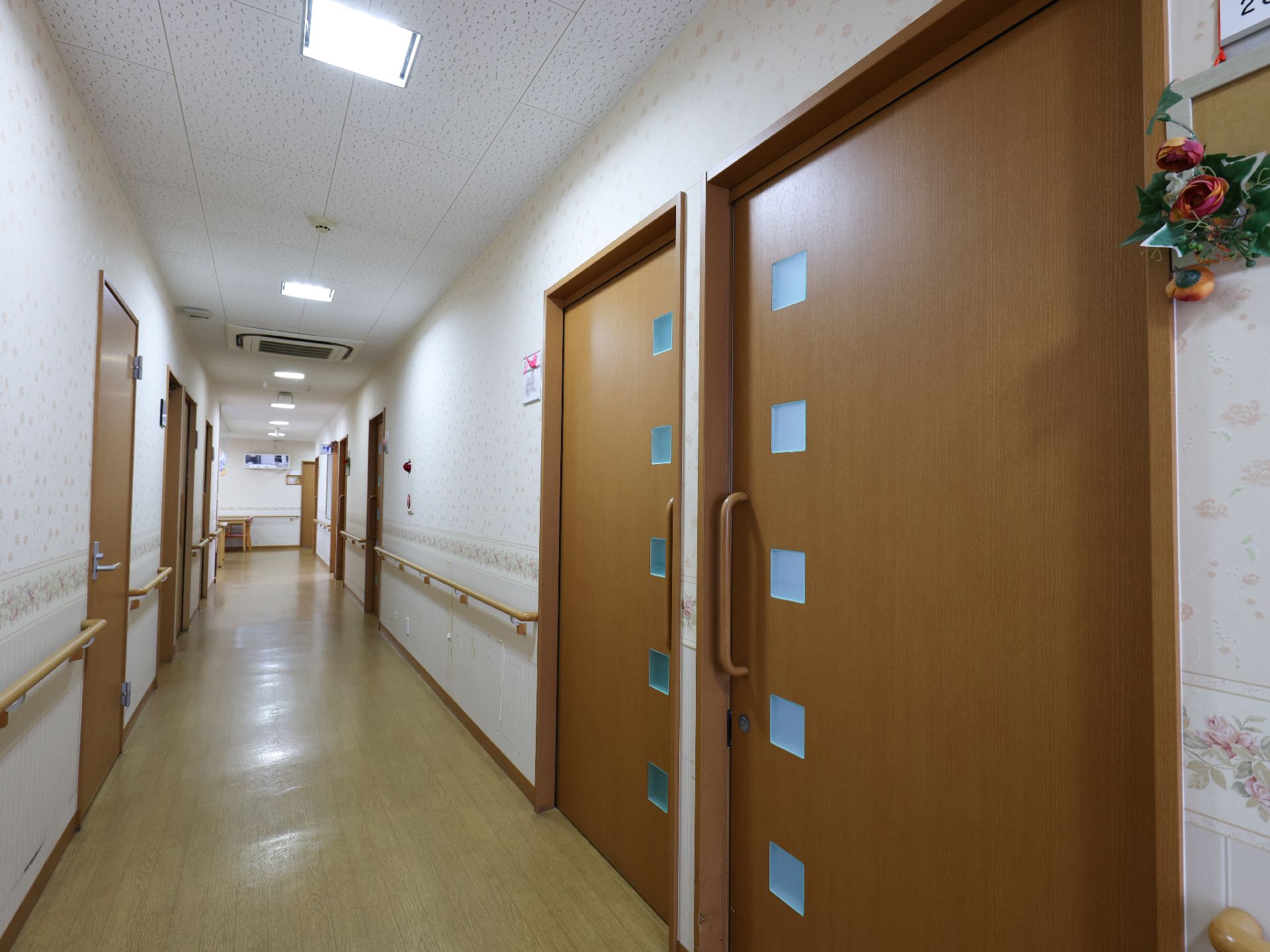 日当たりのいい室内でアジサイの貼り絵をしている高齢女性とエプロンを付けた若い女性スタッフ。