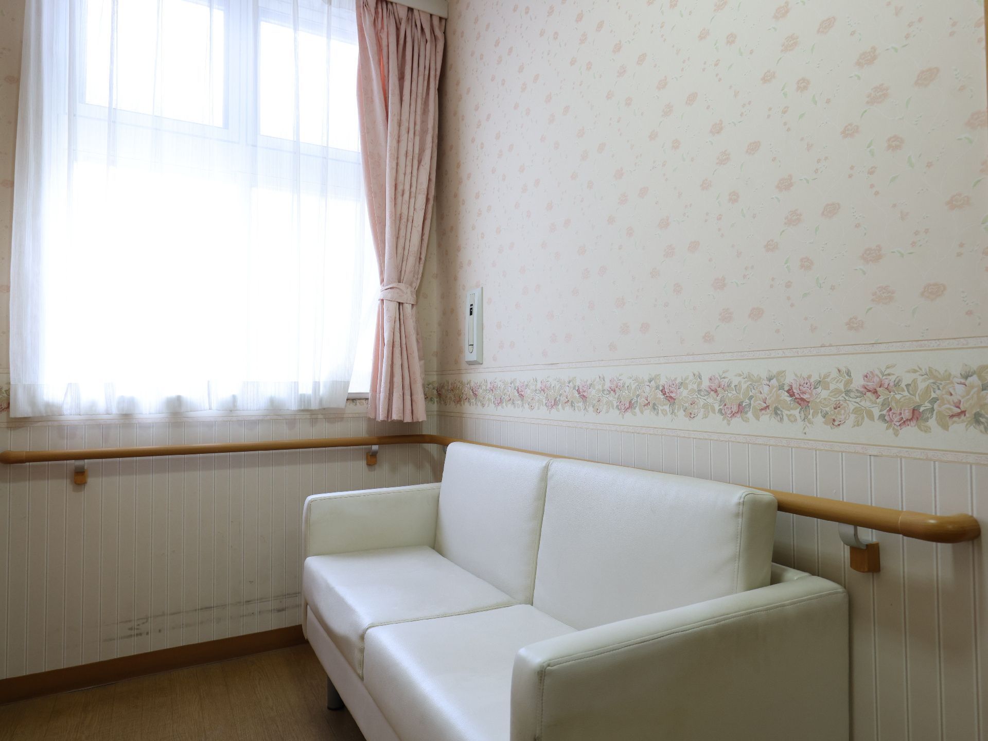 屋外でエプロンを付けた若い女性スタッフが笑顔で車いすの高齢女性に寄り添っている。