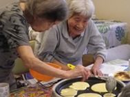 ホットケーキ作りを楽しむ二人の女性入居者。ホットプレートにはまだ焼けていないホットケーキがいくもある。