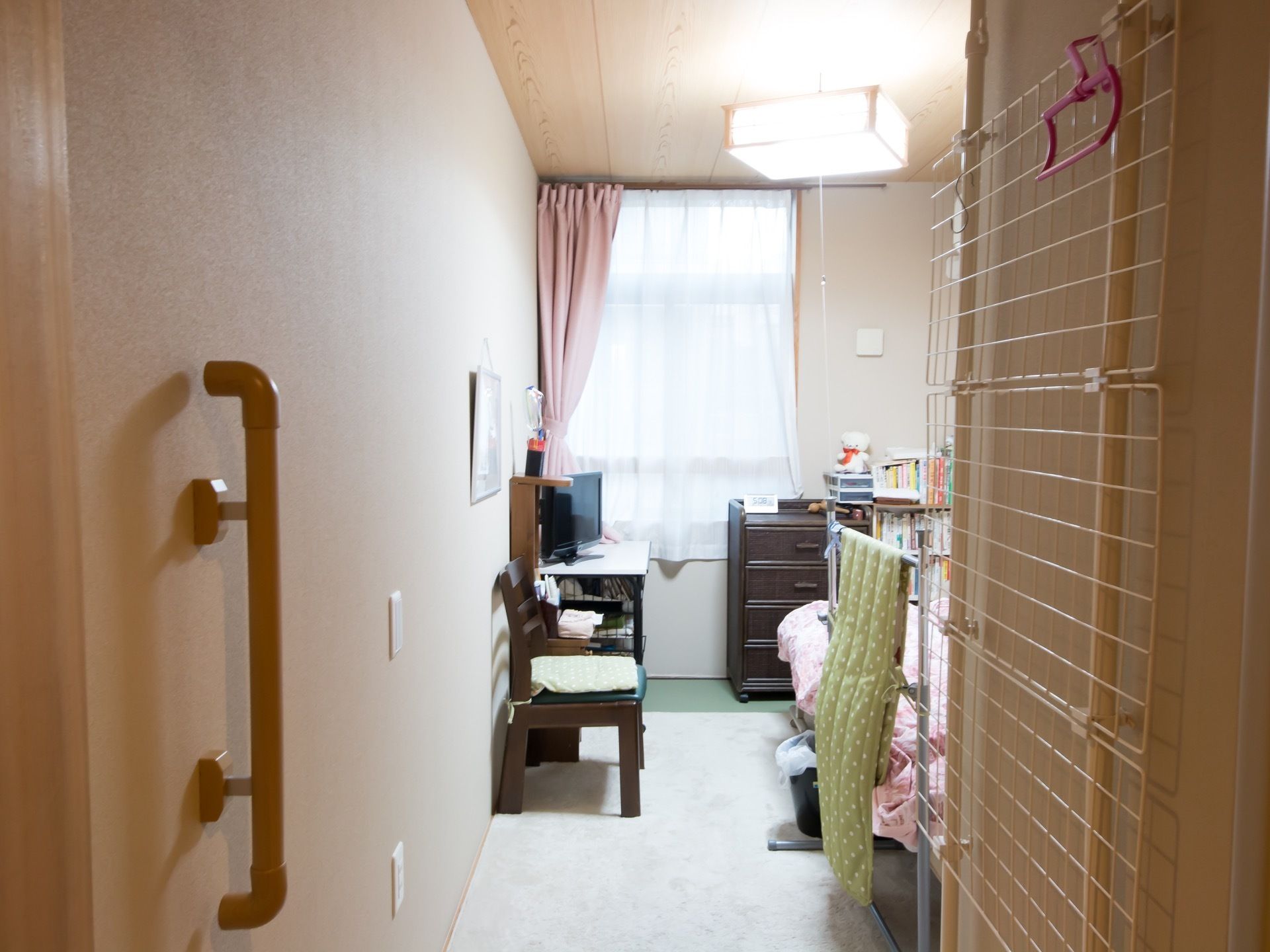 居室には窓があり、レースと薄いピンク色のカーテンがかけられている。ベッドの傍には本棚やタンス、テレビが置かれている。