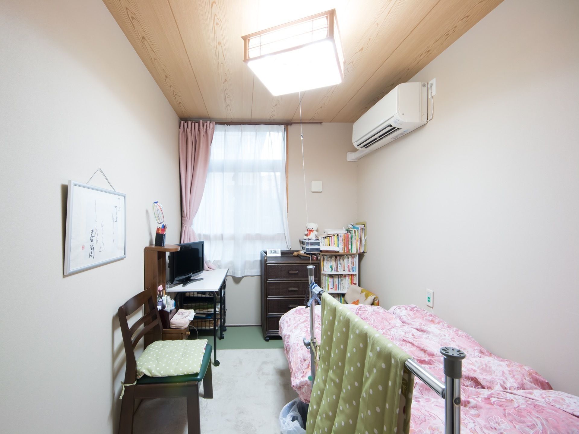 レトロな照明カバーとダークブラウンの家具が落ち着いた雰囲気の室内。壁際にベッドがあり、傍にナースコールが設置されている。