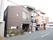 どっしりとした印象を受ける焦げ茶色の外壁をした、木造造り２階建ての建物。道路に面した壁際に花壇が作られている。