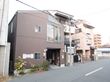 どっしりとした印象を受ける焦げ茶色の外壁をした、木造造り２階建ての建物。道路に面した壁際に花壇が作られている。
