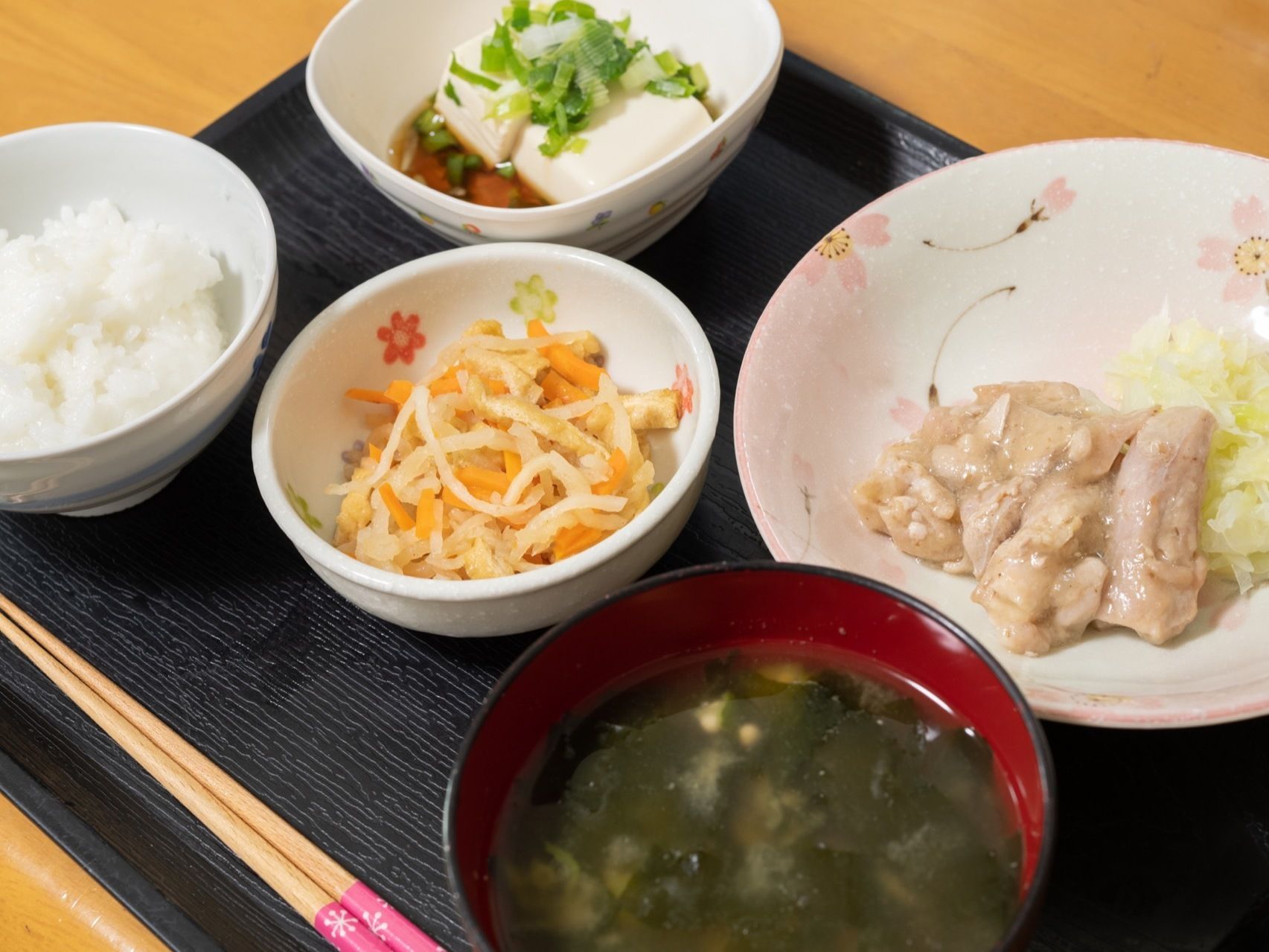 食事は四角いお盆の上に乗せて一人ずつ配膳されている。ご飯に汁物、メインのおかずと小鉢が２つついている。手前にお箸もある。