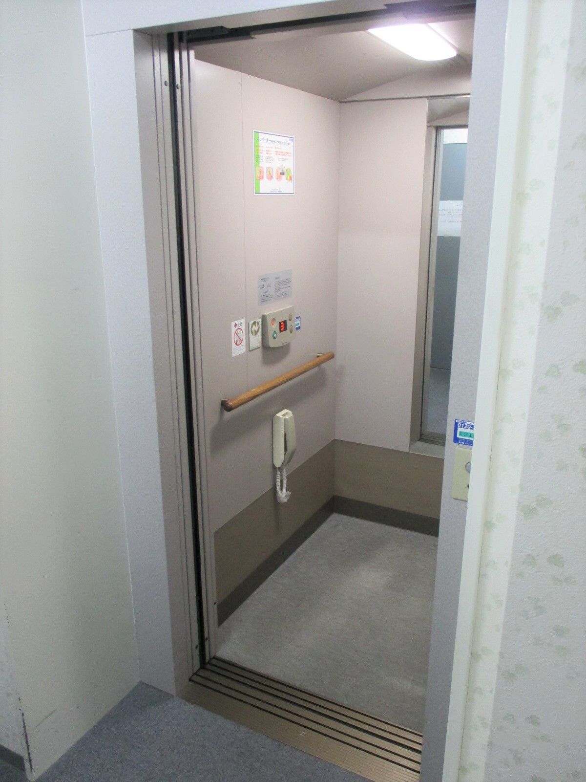 グレーのエレベーターの横には小さなボタンが付き、花柄のクロスが貼られている。