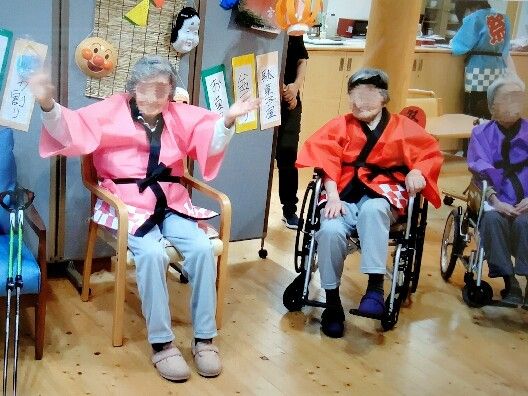 廊下で男性スタッフに抱き着くような姿勢で歩行訓練をしている背の低い高齢女性。