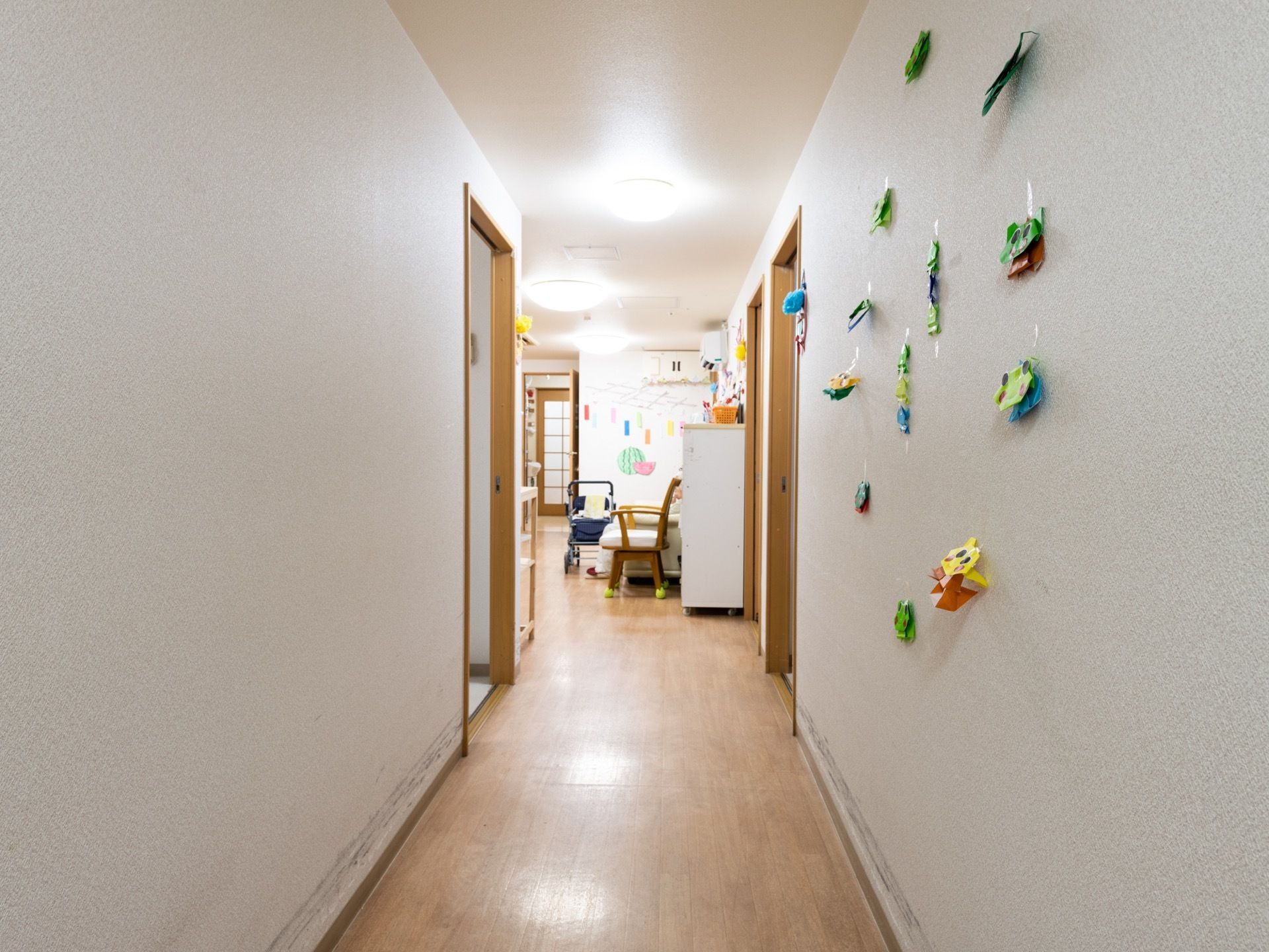 白い壁とベージュ色のフローリングで統一された廊下は、奥の部屋へと繋がっている。壁には、折り紙で折られた飾りが貼られている。