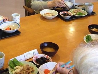 味噌汁、ごはん、おかずが乗ったトレーと、ご飯を食べる高齢者の手元