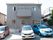 グレーの２階建ての建物の前に、車が複数停めてある。１階の出入口付近には、赤い三角コーンが１つ置かれている。
