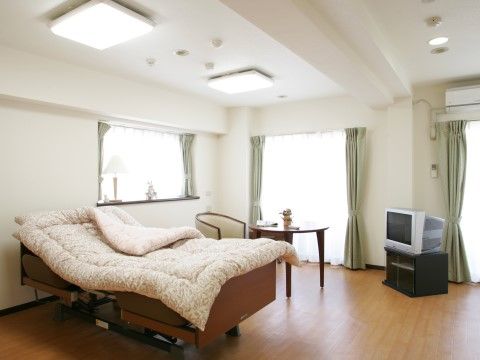 広々としており自由度の高い居室。エアコンがついており、窓際にランプが置かれている。丸テーブルと一人がけのソファが設置されている。