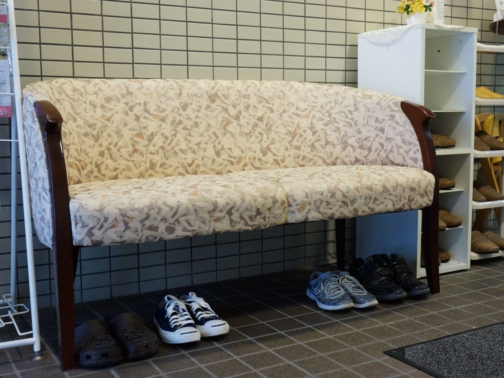 エントランスの椅子は３人ほどの人が座れて、ソファーというよりベンチのような雰囲気である。両隣にはスリッパ棚と、パンフレットホルダーがある。