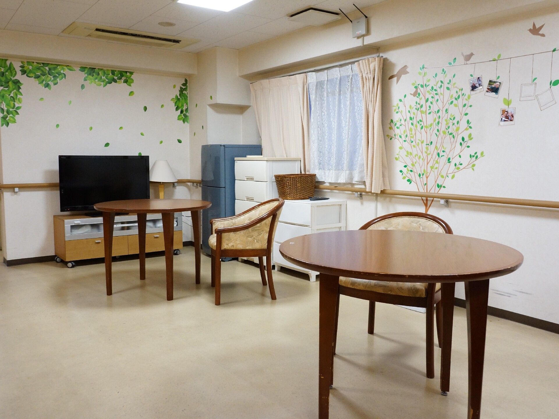 壁に鳥や緑が描かれている、テレビや冷蔵庫が設置されたリビング