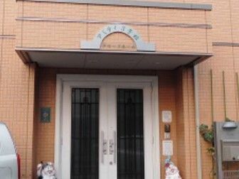 ブラウン系の外観の建物の玄関にはポストやインターホンが設置され、屋根にはホーム名が書かれている。
