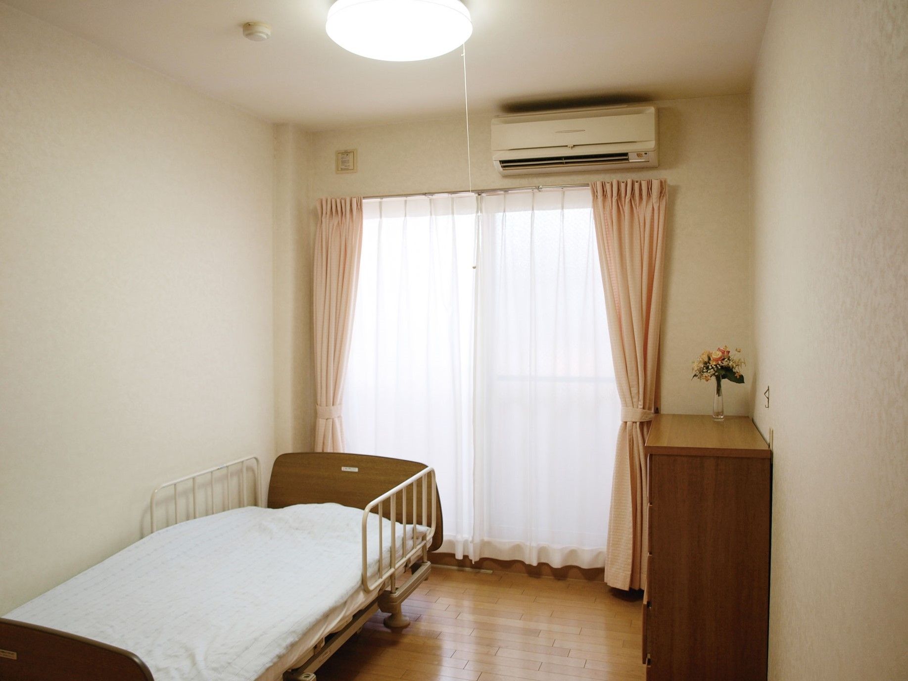 介護用ベッドが置かれており、タンスの上に花が飾られている部屋