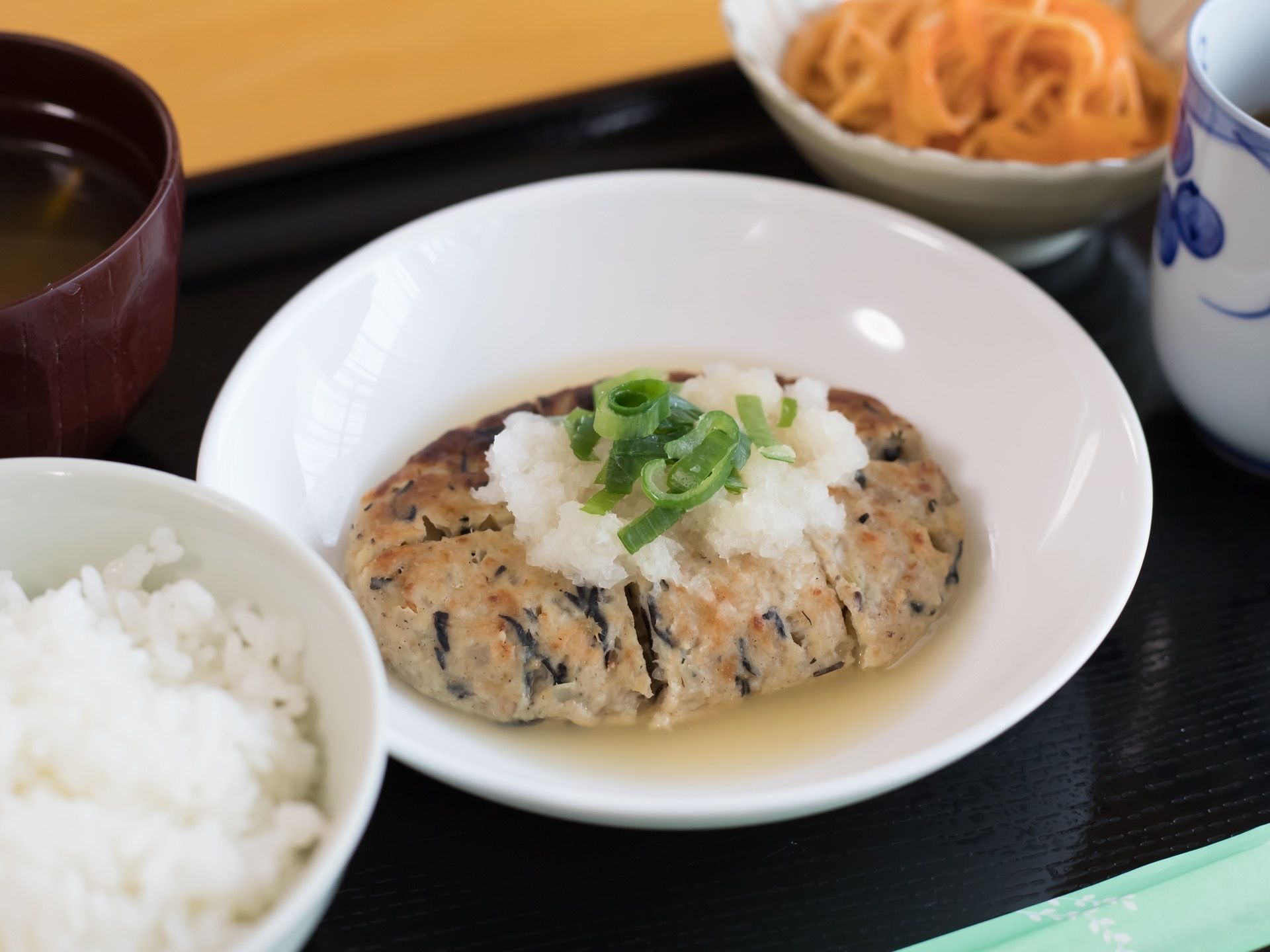 黒いお盆に料理がバランスよく配置されている。今日の食事は、ひじきが入ったハンバーグをメインとした和食である。