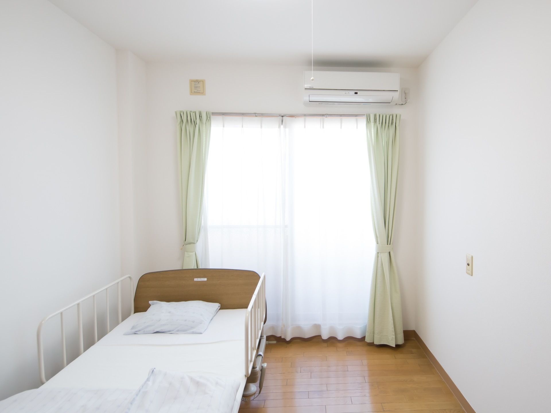 清潔感あふれる、白色を基調とした居室である。掃き出し窓を完備。さわやかなグリーンのカーテンがセットされている。