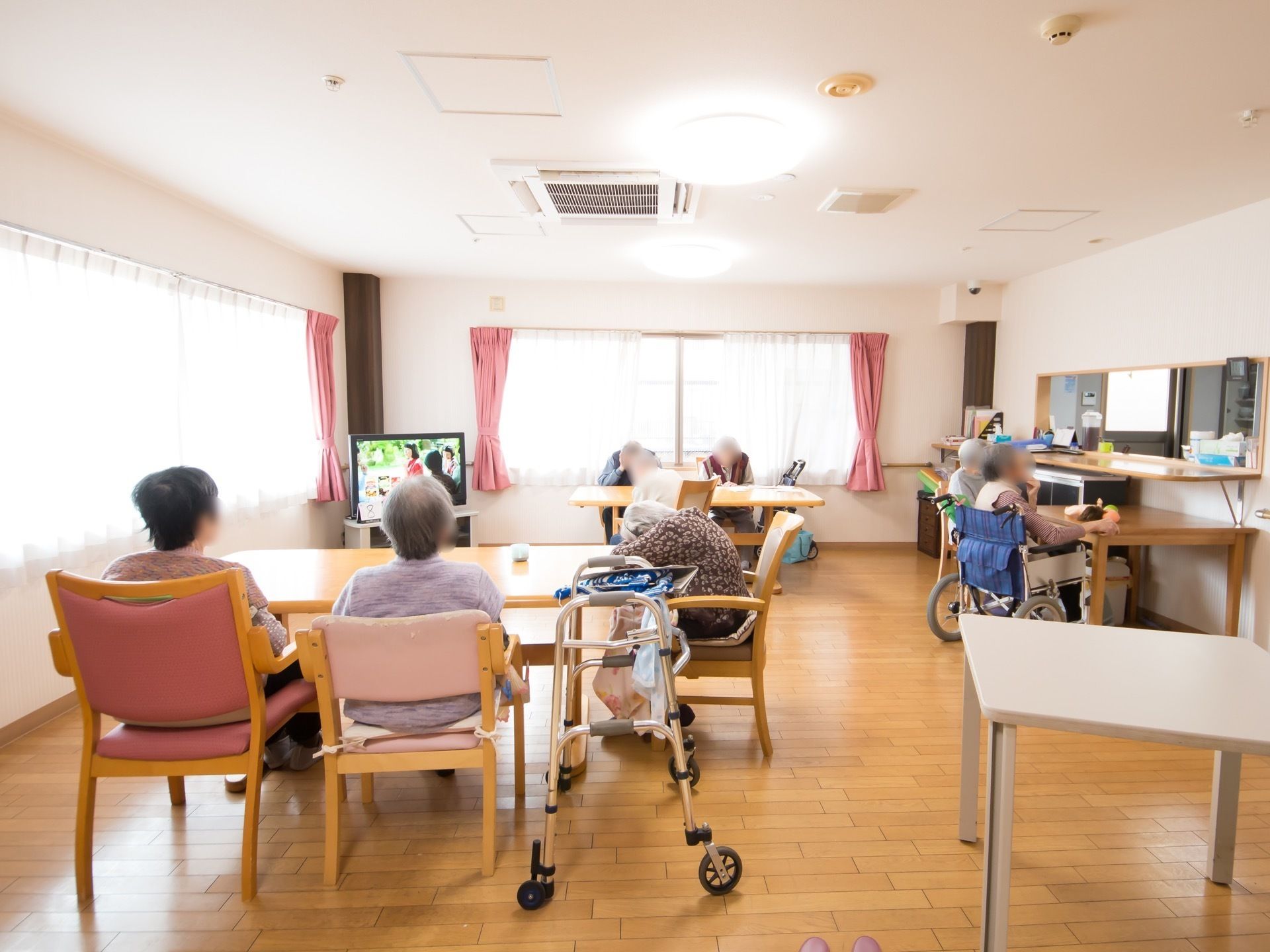 窓に備えつけられた、ピンク色のカーテンがアクセントになっている。入居者様同士が集い、テレビ鑑賞を楽しんでいる。