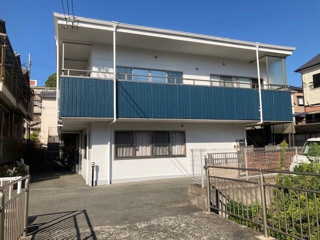 閑静な住宅地に建つ、２階建ての施設である。近くには川が流れており、橋にはグリーンのフェンスが設置されている。