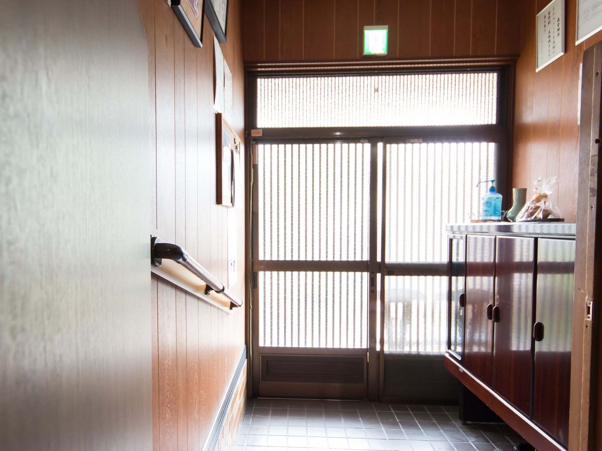 玄関は縦に格子のついた引き違い戸である。壁は縦長の板からなり、一本の手すりが設置してある。和風な靴箱もついている。