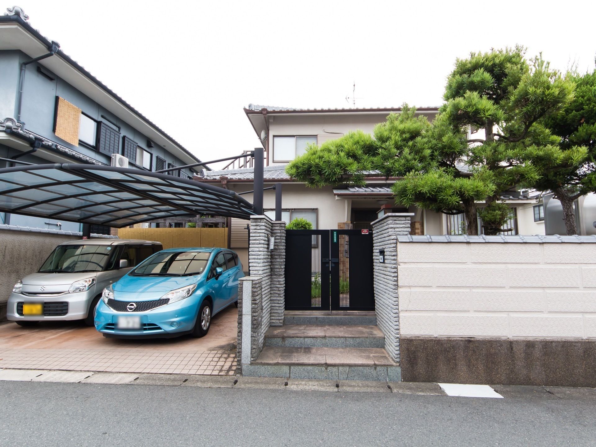 庭にある松の木が塀越しに見えており、外観は２階建ての一軒家である。駐車場に湾曲した屋根が付いている。