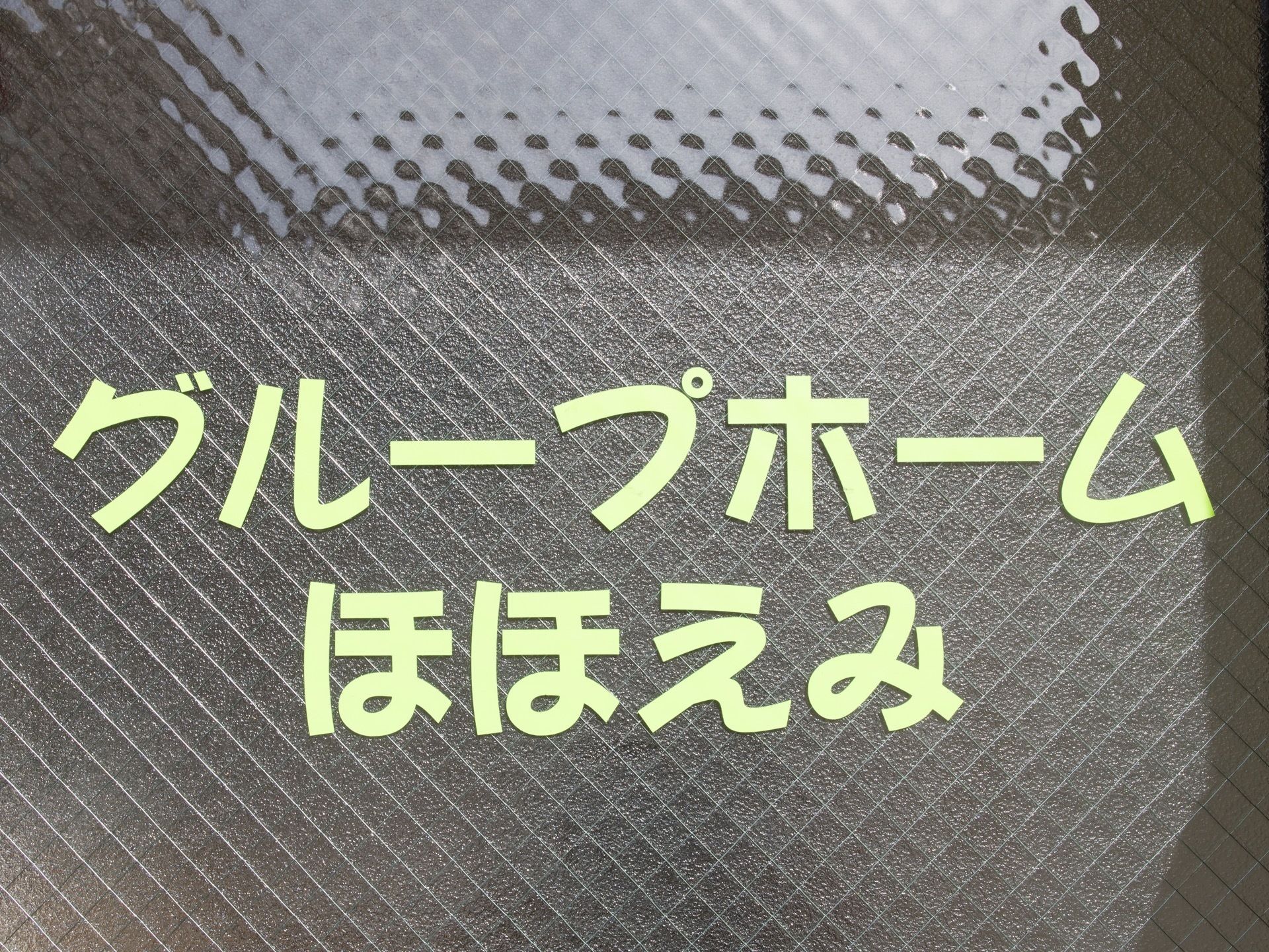 施設の窓ガラスに施設名が表示されている。飛散防止のワイヤーが入ったガラスに、かわいらしいフォントで書かれている。